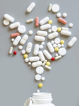 Mix of medical capsules and pills fall out of a bottle on grey top view. Medicinal treatment. Taking dietary supplements and vitamins. Assorted pharmaceutical products