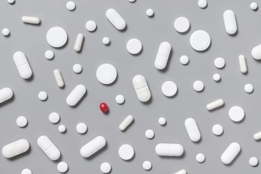 Mix of white medical capsules and pills with one red on grey top view. Preventive medicine and healthcare, taking dietary supplements. Assorted pharmaceutical medicine capsules