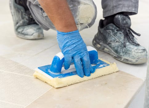 Craftsman washing surface with a float sitting on hes knees. Men in grey work clothes outside during construction or renovation process