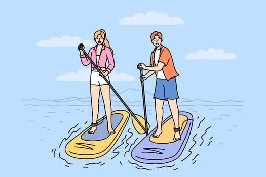 Surfing on SUP boards is practiced by man and woman using paddles to navigate river on summer weekend. Man and woman surfers stand on SUP boards, engage in active recreation at hot resort
