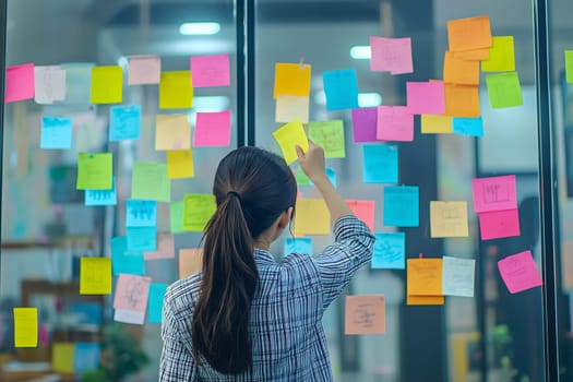 Female business professional analyzing colorful sticky notes on a glass board for project planning in a modern office setting