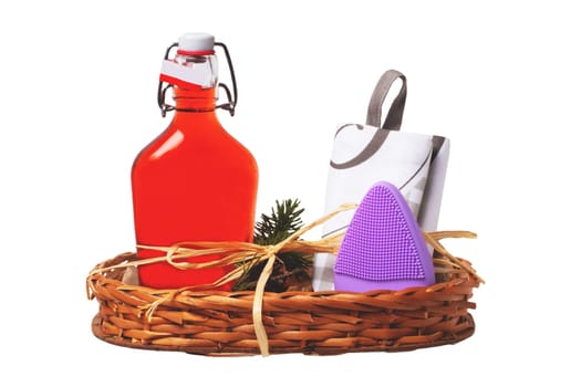 Closeup of a gift basket with swing top bottle with red alcohol, a folded shopping bag and a silicone brush for facial cleansing with massage vibration isolated on white