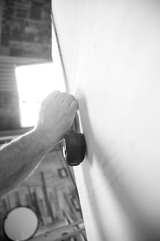 Black and white image of A carpenter is using a tape measure to check the dimensions of a large wooden plank while working in his workshop