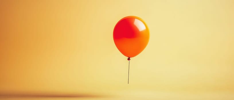 A vibrant orange balloon is suspended in mid air contrasting beautifully with a soft yellow background creating a cheerful atmosphere.