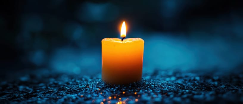A yellow candle burns gently in a darkened space casting a warm glow over a reflective surface creating a tranquil atmosphere.
