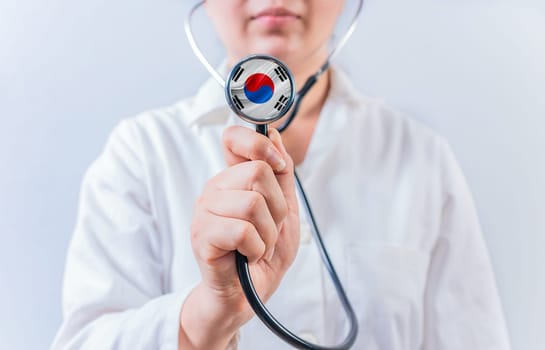 Female doctor holding stethoscope with South Korean flag. South Korean Health and Care concept
