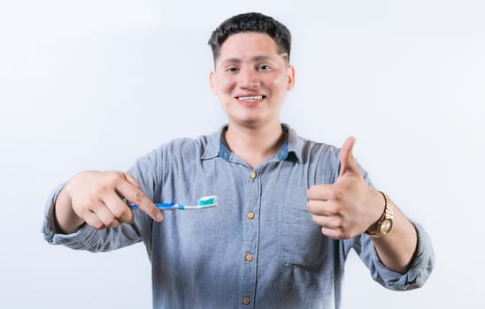 Smiling young man holding a toothbrush gesturing OK. Person holding toothbrush with thumbs up. Guy holding a toothbrush with OK gesture