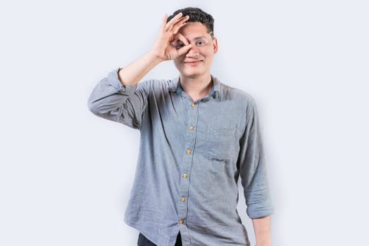 Happy young man making ok gesture with hand looking through fingers. Smiling person making ok gesture looking through fingers isolated