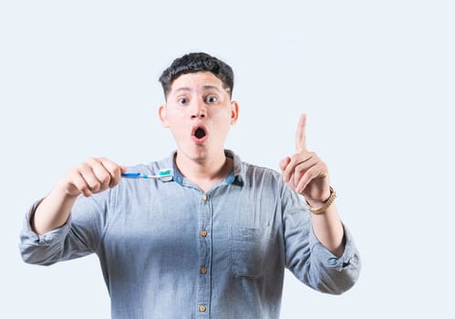 Surprised young man holding toothbrush pointing up isolated. Amazed man with toothbrush pointing up advertising