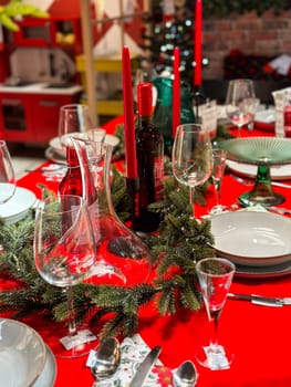 Christmas set table is adorned with festive decorations, ready for a joyful winter holiday gathering. Vibrant red tablecloth and elegant tableware create a warm and inviting atmosphere.