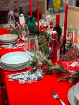 Christmas set table is adorned with festive decorations, ready for a joyful winter holiday gathering. Vibrant red tablecloth and elegant tableware create a warm and inviting atmosphere.