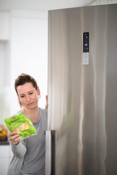 Pretty, young woman taking groceries out of the fridge, checking the dates, healthy eating concept, household lifestyle concept