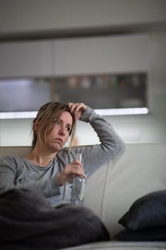 Midlle aged woman at home with a bottle of strong alcohol in her hands, dealing with depression, pain, loneliness