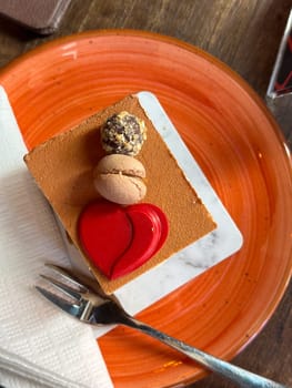 Close-up of a delicious chocolate mousse cake with macaron and truffle topping on an orange plate. Concept of indulgence and delight sweets in a cozy cafe setting