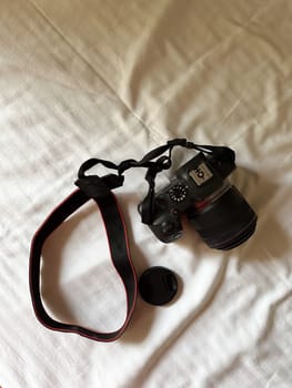 Camera with a strap placed on a white bed sheet, capturing the essence of travel preparation and creativity. Simplicity, creative and readiness of a photographer journey.