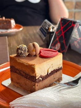Close-up of a delicious chocolate mousse cake with macaron and truffle topping on an orange plate. Concept of indulgence and delight sweets in a cozy cafe setting