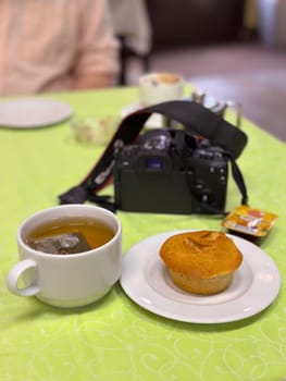 Cozy cafe setting with a cup of tea, a muffin, and a camera on a green table. Harmony of relaxation, creativity and indulgence.