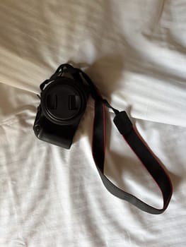 Camera with a strap placed on a white bed sheet, capturing the essence of travel preparation and creativity. Simplicity, creative and readiness of a photographer journey.