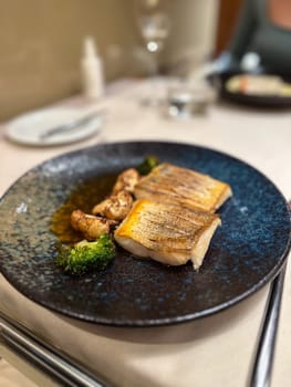 Plated gourmet dish features succulent fish fillets accompanied by roasted cauliflower and broccoli, set against a rich, dark sauce. this image captures an exquisite dining experience, showcasing the artistry of haute cuisine.