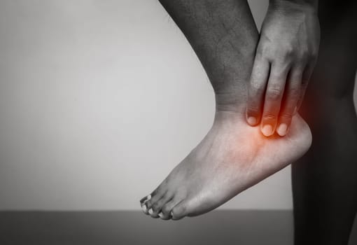 Woman with acute pain ankle with leg pain on gray background, Ankle and leg treatment, Female massaging her ankle muscle spasm, Healthcare and medical concept, Injuries and medical concept.