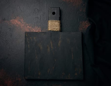 Empty black wooden cutting board and linen kitchen towel, top view. Copy space