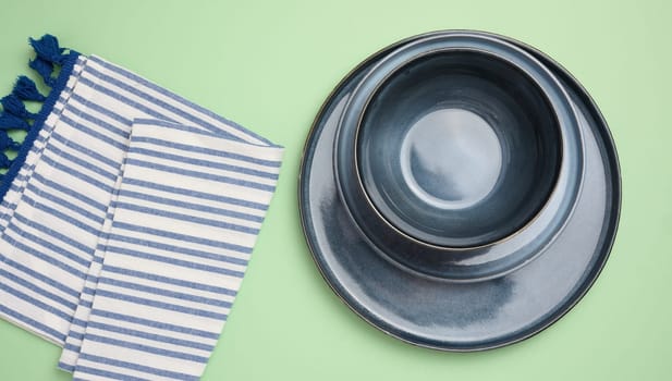 Empty round ceramic plate and kitchen towel on green background, top view