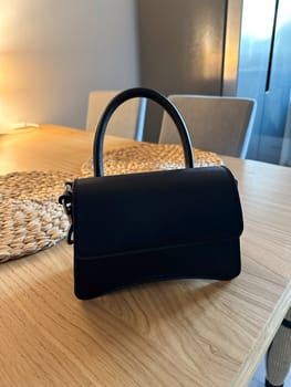Stylish fashion black handbag placed elegantly on a wooden table. Soft lighting creates a warm atmosphere, highlighting the design and texture of the purse.