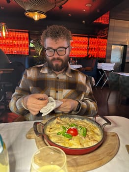 Millennial man enjoying a delicious meal in a stylish restaurant setting. Vibrant red backdrop and beautifully plated dish create a warm and inviting dining atmosphere.