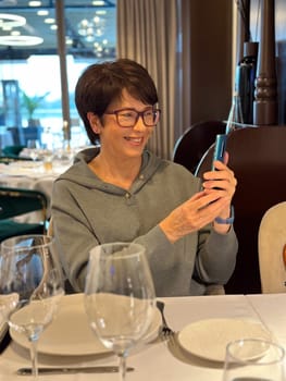 Woman in a cozy sweater using her smartphone take photo while seated at a table in a stylish restaurant. Elegantly dinner. Blog, blogger and influencer in social networks concept.