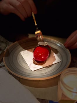 Close-up gourmet dessert with red glaze and chocolate decoration served on a plate, ready to be enjoyed in a cozy restaurant.