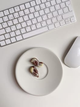 Top view white workspace with keyboard and plate of chocolates. The clean, minimal design emphasizes a blend of work.