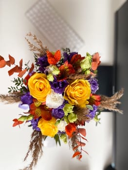 Colorful bouquet of flowers in a lavender box standing on a desk, tied with a vibrant red and purple ribbon. Bright, mixed arrangement adds a touch of nature and warmth to modern workspace.