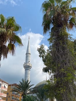 Stunning blend of palm trees and a mosque tower against a backdrop of city life and tranquil skies. Cultural architecture in an urban setting.
