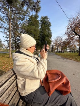 Woman taking a photo in a park on a sunny autumn day, moments of leisure and connection with nature amidst fall cold scenery.