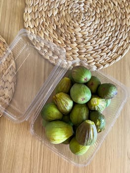 Container filled with fresh figs placed on a natural woven mat. Green fruits offer a glimpse into healthy eating and the beauty of seasonal produce.