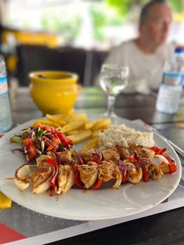 Delicious plate of grilled chicken skewers with rice, salad, and fries on a wooden table setting. Well-balanced and colorful meal, perfect for a vibrant dining experience.