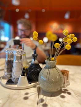Table with decorative vase and condiment set in cozy restaurant ambiance. Warmth and elegance of a dining table setting, highlighting the intricate details of the decorations.