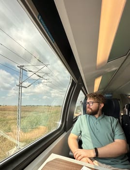 Man traveler enjoying a serene view from a train window. Calm and reflection during a peaceful journey.