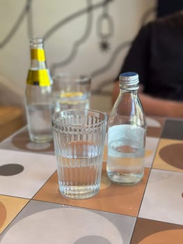 Glass of water alongside a bottle on a patterned tile table. Depicting everyday hydration and minimalistic lifestyle themes