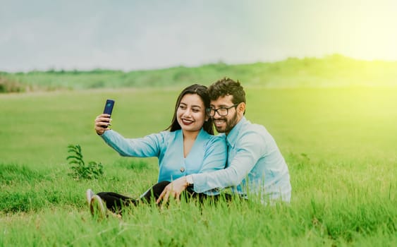 Smiling young couple in love taking a selfie sitting in the field. Happy Couple in love taking a selfie sitting in a beautiful field