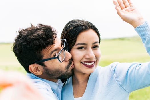 Selfie of young happy couple kissing in the field. Cute couple in love taking a selfie in the field, looking at the camera