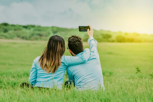 Couple in love taking a selfie sitting in a beautiful field. Young happy couple taking a selfie sitting in the field