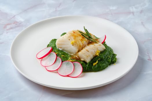 A beautiful presentation of a fish fillet garnished with herbs lies atop a smooth spinach puree, complemented by thin slices of radish for a touch of freshness and color, making it an enticing dish.