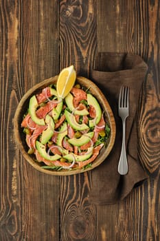 Overhead view of salad with fresh salmon, avocado and onion served in a wooden bowl on a rustic wooden table