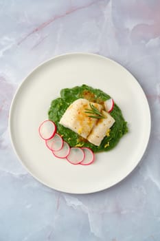 Tender white cod fish atop a smooth spinach puree, accompanied by thinly sliced radishes. The arrangement highlights freshness and culinary artistry.