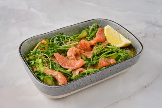 A vibrant salad features fresh smoked salmon slices mixed with crisp arugula and cucumber, garnished with a lemon wedge for a zesty touch, presented in a stylish serving platter.