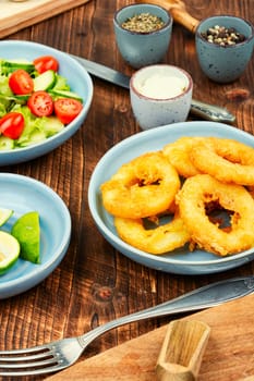 Serving of calamari, deep-fried squid rings, garnished with vegetable salad. Close up.