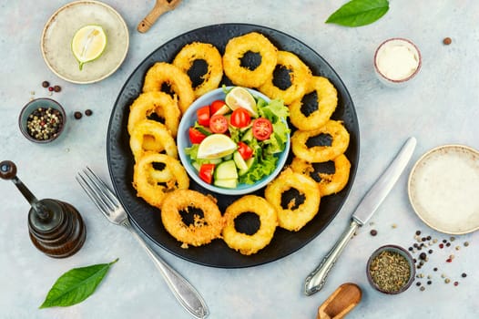 Serving of calamari, deep-fried squid rings, garnished with vegetable salad. Close up.