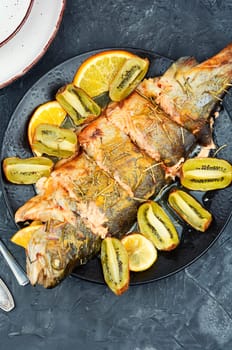 Roasted fish is served with kiwi slices and orange. Seafood dinner, fried trout, healthy dish.