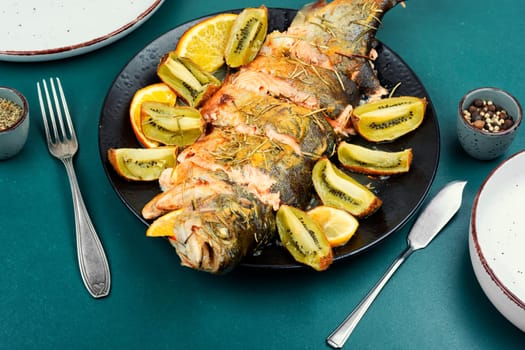 Roasted fish is served with kiwi slices and orange. Seafood dinner, fried trout, healthy dish.